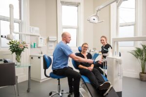 Dentista mostrando resultado do tratamento de prótese protocolo para paciente sorrindo em consultório